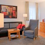Wohnzimmer mit Sofa, Sessel, Couchtisch und Wandbild.