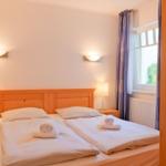 Doppelbett mit weißen Laken, zwei Nachttische und Fenster mit Vorhängen.