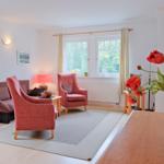 Wohnzimmer mit Sofa, zwei Sesseln, Fenster und Blumen.