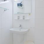 Badezimmer mit Waschbecken, Spiegel und Glasregal an der Wand.