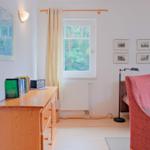 Ein Raum mit Fenster, Sofa, Stuhl und Schrank. An der Wand hängen Bilder.