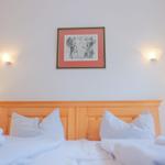 Schlafzimmer mit Holzbett, weißen Kissen und Wandbild.