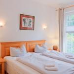 Ein Schlafzimmer mit Doppelbett, zwei Nachttischen und einem Fenster mit Blick auf Balkon.