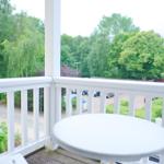 Terrasse mit weißem Tisch und Stühlen. Blick auf grüne Bäume und Parkplatz.