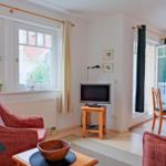 Wohn- und Essbereich mit TV, Sitzgelegenheiten und Balkontür.