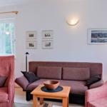 Ein Wohnzimmer mit Sofa und zwei Sesseln, Tisch und Fenster.