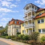 Ferienhaus mit Balkonen und rotem Dach, Strandweg und Bäume im Hintergrund.