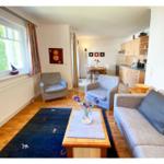 Wohnzimmer mit Sofa, zwei Sesseln und Küchenbereich im Hintergrund.