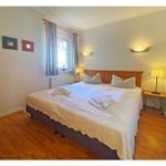 Schlafzimmer mit Doppelbett, Holzboden und Fenster mit Vorhängen.