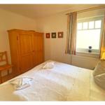 Schlafzimmer mit Bett, Holzschrank und Fenster mit Vorhängen.