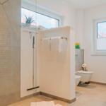 Badezimmer mit Dusche, Toilette und Waschbecken. Fenster mit Blick auf Dächer.