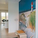 Eingangsbereich mit Wandbild eines Leuchtturms und Holzbank mit Kissen.