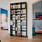 Großer Bücherregal trennt Wohn- und Schlafbereich. Schlafzimmer mit Bett und Wandbild.