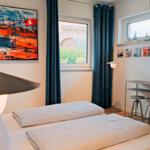 Schlafzimmer mit Bett, Fenster, Tisch und Wandbild.