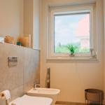 Badezimmer mit Toilette, Bidet und Fenster mit Blick auf Dach und Grün.