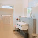 Badezimmer mit Waschbecken, Spiegel und Handtuchhalter. Fenster und kleine Sitzgelegenheit.