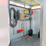 Garderobe mit Werkzeug, Besen und Boxen an der Wand.