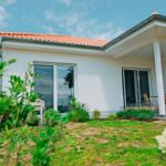 Wohnhaus mit Terrasse, Gartentüren und Garten. Weiße Fassade und rote Ziegeldach.
