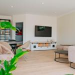 Wohnzimmer mit Sofa, Fernseher und Essbereich. Holzboden und Pflanzen sichtbar.