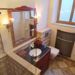 Badezimmer mit Waschbecken, Spiegel und Toilette. Steinfliesen und Holzrahmen.