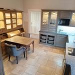 Küche mit Essbereich, grauen Schränken und Steinplattenboden.