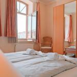 Zimmer mit Doppelbett, Fenster, Gardinen und Spiegelschrank.