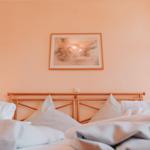 Ein Bett mit weißen Kissen und Decken, Wandbild und Vorhang.
