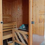 Holzsauna mit Bänken und Steinen. Tür offen, Blick ins Innere.