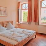 Schlafzimmer mit Doppelbett, zwei Fenstern und Terrakottaboden.