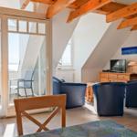 Wohnraum mit blauen Sesseln, Holzbalken und Blick auf den Hafen.