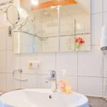 Badezimmer mit Waschbecken, Spiegel, Dusche und Haartrockner.