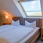 Schlafzimmer mit Dachschrägen, Bett mit weißen Laken und zwei Nachttischen mit Lampen.