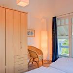 Schlafzimmer mit Doppelbett, Kleiderschrank und Blick auf Balkon.