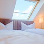 Doppelbett mit weißen Kissen unter Dachfenster mit Blick auf Himmel