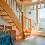 Holztreppe führt zur Terrasse mit Blick auf Hafen. Tisch mit Stühlen und Korb unter der Treppe.