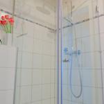 Dusche mit Glaswand, weißen Fliesen und roten Tulpen.