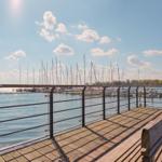 Holzterrasse mit Blick auf Hafen und Segelboote unter blauem Himmel.