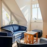 Wohnzimmer mit blauem Sofa, zwei Sesseln und Holztisch unter Dachschrägen.