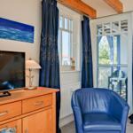 Ein Wohnzimmer mit blauem Sessel, TV und Blick auf die Terrasse.