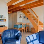 Wohn- und Essbereich mit Holzstufen, blauen Sesseln und Tisch mit Stühlen.