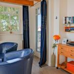 Zwei blaue Sessel stehen vor Fenstern mit dunkelblauen Vorhängen. Holzregale und ein Tisch sind sichtbar.