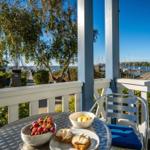 Tisch mit Obst und Brötchen auf Terrasse mit Blick auf Hafen und Bäume.
