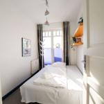 Ein Schlafzimmer mit weißem Bett, Fenster und Wandregal.