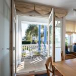 Durchgehendes Fenster mit Blick auf Terrasse mit Tisch und Stühlen. Wohnzimmer mit Sofa und Esstisch.