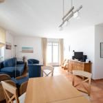 Wohn- und Essbereich mit blauer Couch, Holztisch und Terrassentür.