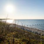 Strand mit Steinen, blauen Strandkörben und Sonne am Horizont.
