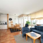 Wohnbereich mit Sofa, Esstisch und Küchenzeile. Fenster mit Blick aufs Meer.