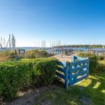 Blauer Holzzaun führt zu einem Bootssteg mit Yachten und grünen Büschen.