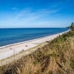 Strand mit Sanddünen, Strandkörben und blauem Meer unter klarem Himmel.