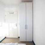 Schlafzimmer mit weißem Kleiderschrank und Bett. Tür mit Haken.